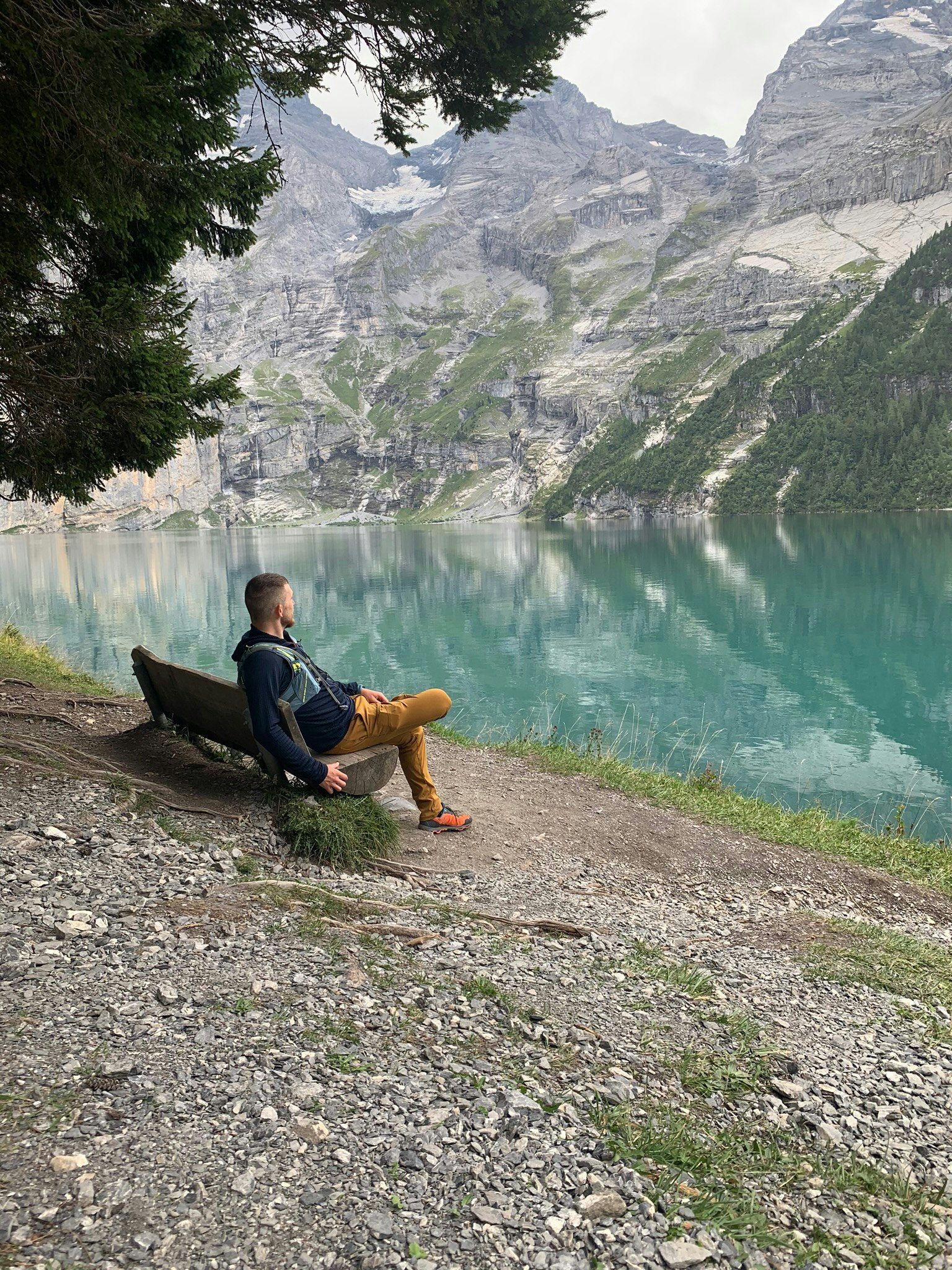 Charlie, sitting on a bench, looking away from the camera and out at a lake in the Swiss Alps
