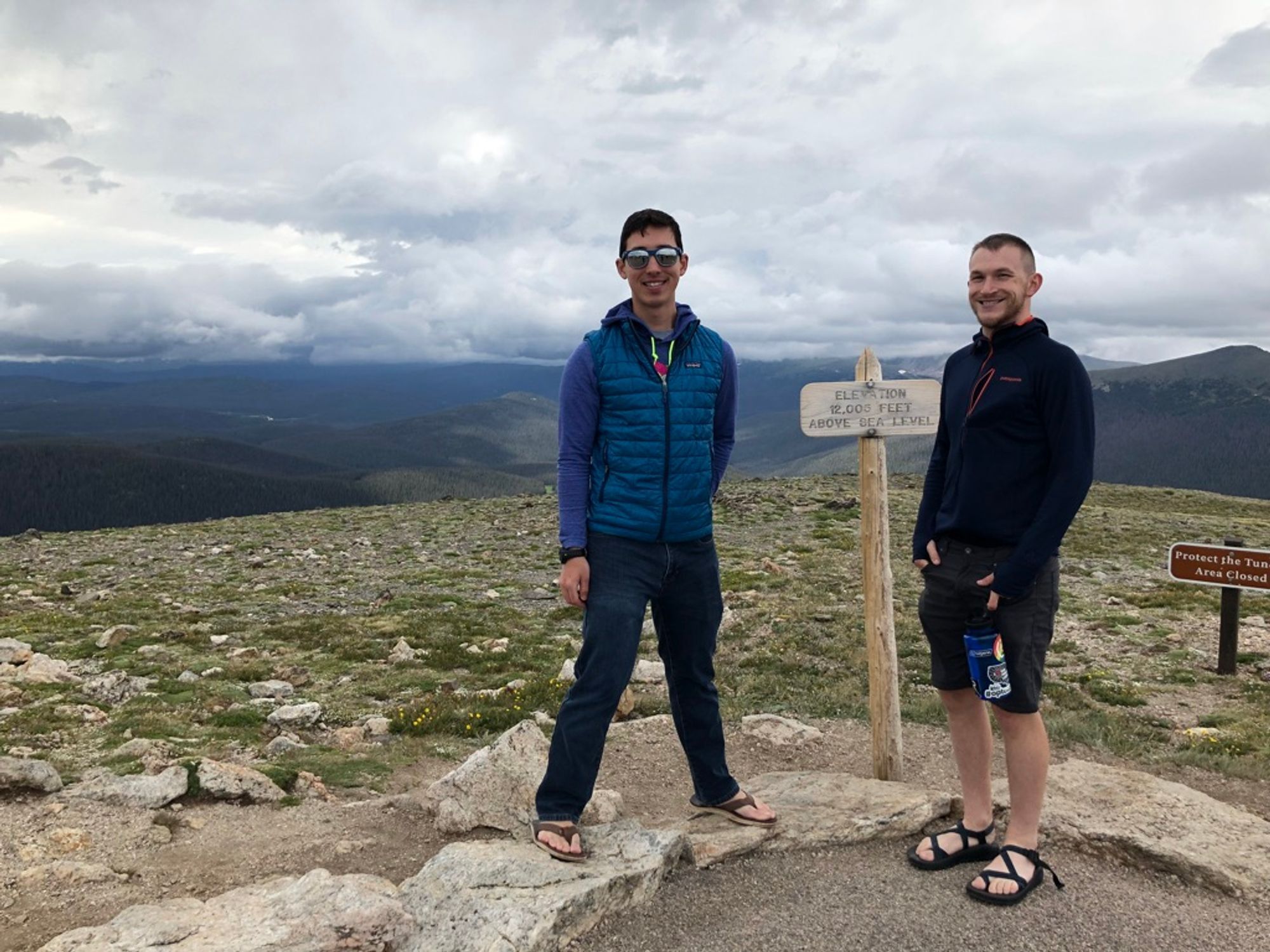 Me and Josh, standing in front of a small sign that says "Elevation 12,003 feet above sea level" with the Rocky Mountains in the background